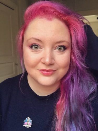 Author Spotlight: Greek Author Danai Christopoulou. Image of a woman with long pink and purple hair, green eyes and wearing a navy sweatshirt.