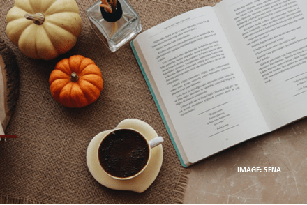 My Greek Books October 2025 Reads. Image of a table with a wite and orange pumpkin, a cup of coffee on a saucer and an open book